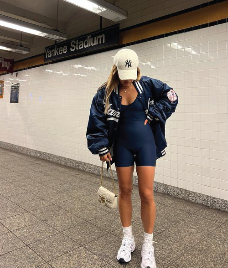 athletic romper layered with stadium jacket, white sneakers, and slouch socks for baseball game