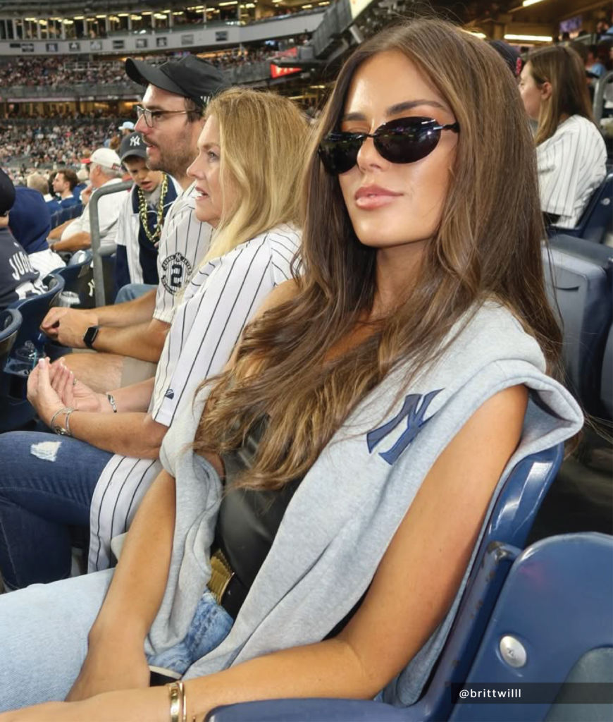 oversized baseball sweatshirt paired with blue jeans and bold sunglasses at stadium
