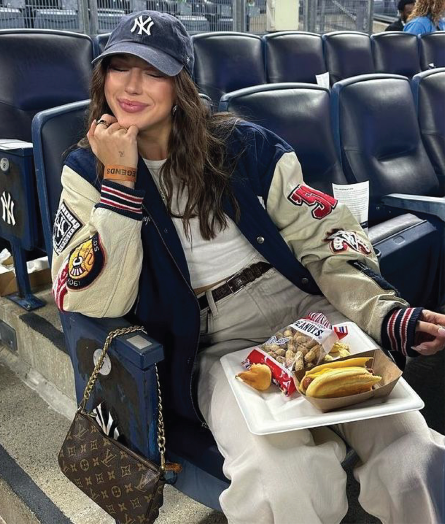 varsity jacket with relaxed trousers tucked tee and baseball cap styled for stadium outfit