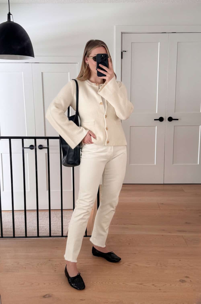 Woman wearing cream denim jeans with a matching cream cardigan, styled with black ballet flats and a dark handbag for contrast.