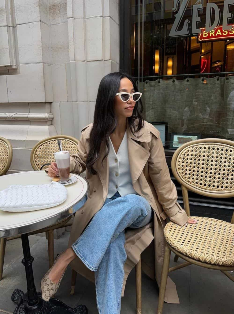 Woman wearing a fitted white vest top with light-wash jeans, styled with kitten heels and a trench coat.