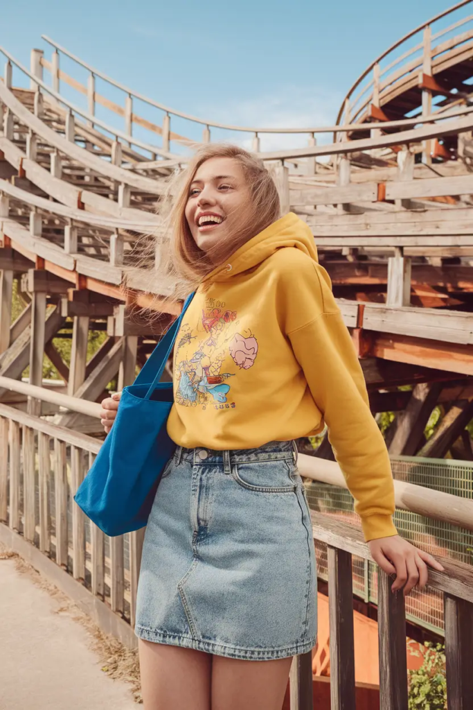 Yellow cartoon hoodie paired with a high-waisted denim mini skirt and casual sneakers for a playful comfy school outfit