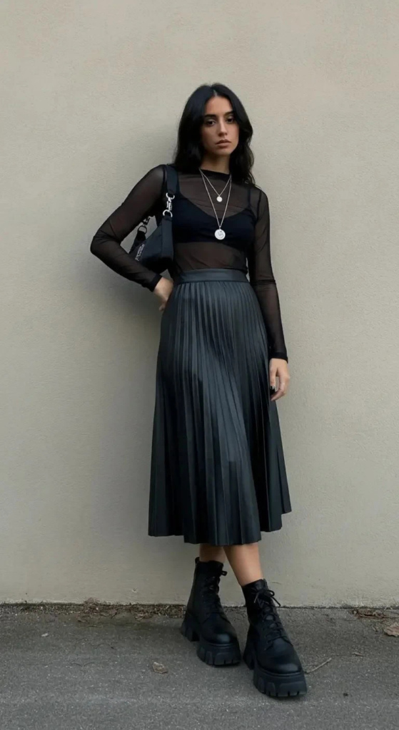 Woman wearing a black leather midi skirt styled with a sheer mesh top and platform boots at a nighttime concert.