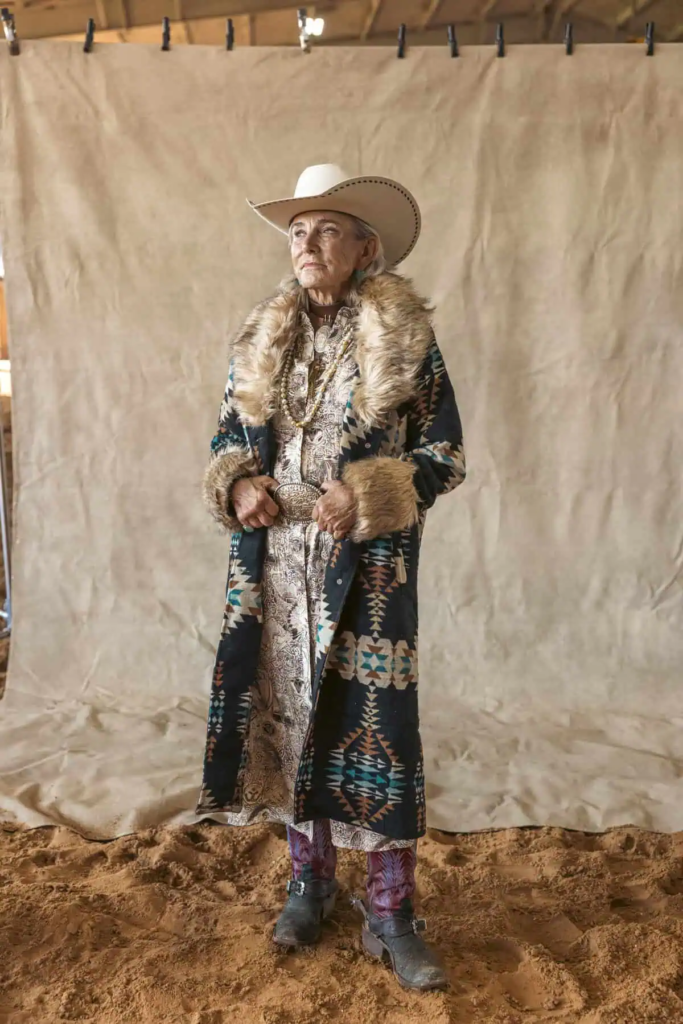 Woman wearing Southwestern-inspired long coat with faux fur trim, patterned midi dress, cowboy boots, and wide-brim hat.
