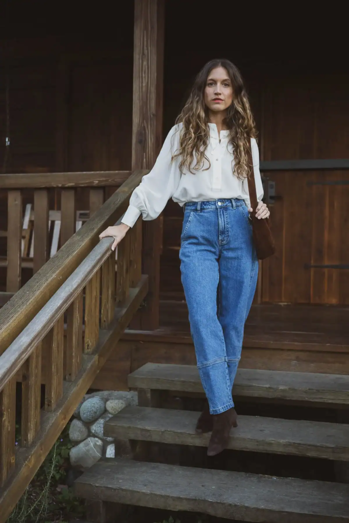 Woman wearing white flowing blouse, high-waisted denim jeans, and brown boots with Western fall vibes.