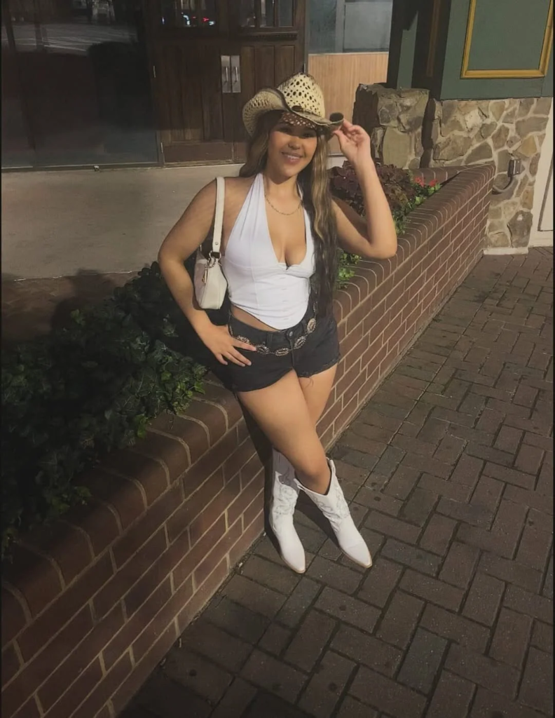 White fitted crop top with black shorts and white cowboy boots styled with a straw cowboy hat for a modern baddie cowgirl outfit.