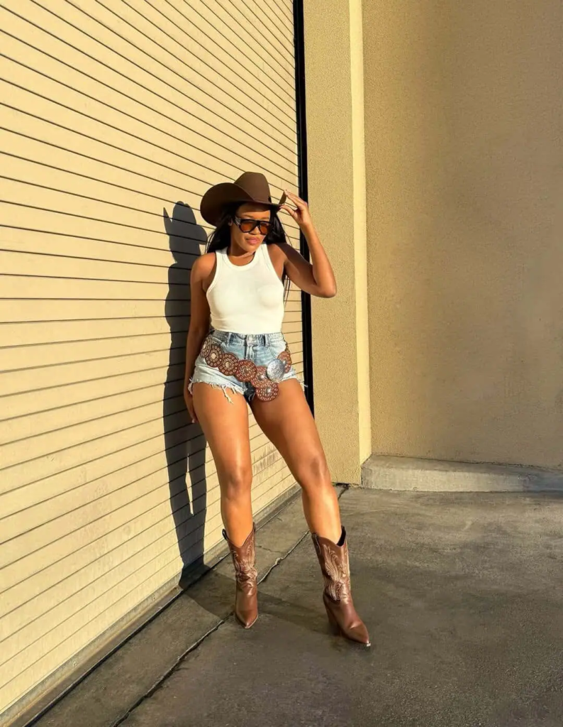 White tank top with embellished denim cutoffs, brown cowboy boots, and brown cowboy hat for a casual baddie cowgirl outfit.