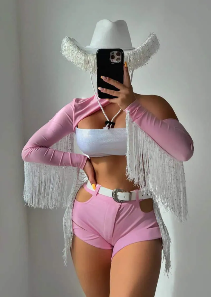 Pastel pink crop top and shorts with fringed white jacket and cowboy hat for a stylish baddie cowgirl outfit.
