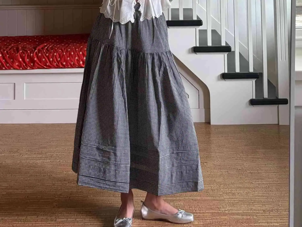 Woman walking through fallen leaves wearing a black-and-white gingham maxi skirt with ruffles, a tucked-in white blouse, and metallic flats.