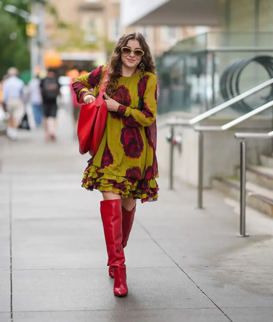 Woman wearing a chartreuse floral dress with burgundy flowers, paired with red knee-high boots and a matching handbag.