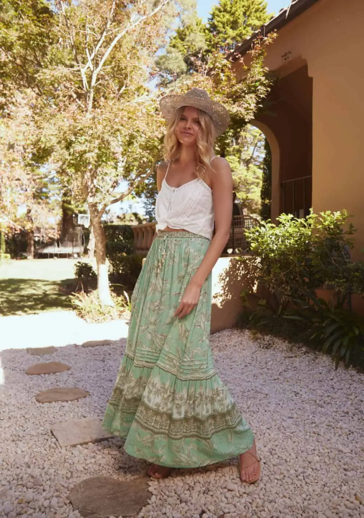 Woman in a mint green floral maxi skirt with a white crop top, accessorized with a woven straw hat and flat sandals.