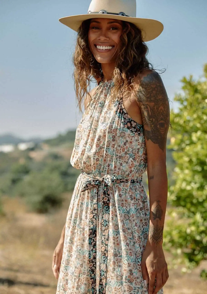 Woman wearing a peach-and-blue floral maxi dress with a belted waist and a wide-brim cream hat.