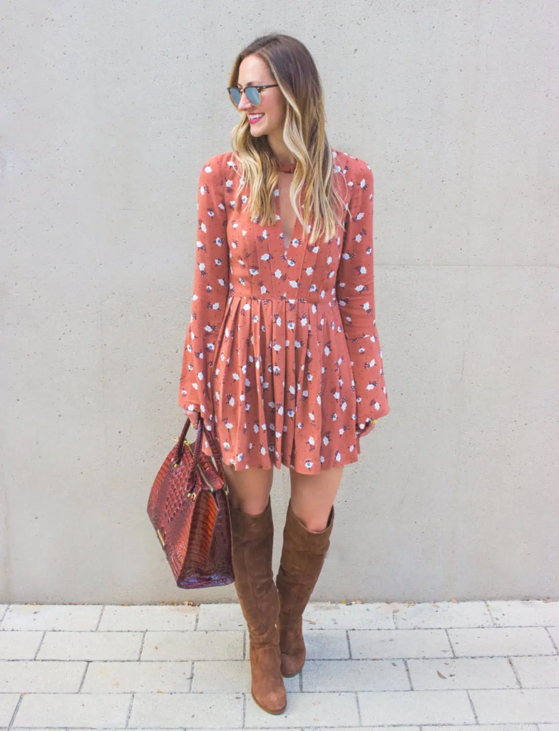 Woman in a rust floral mini dress with bell sleeves, paired with knee-high caramel suede boots and a leather handbag.
