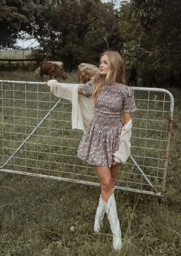 Woman wearing a muted floral mini dress with a cream chunky knit cardigan and white knee-high boots.