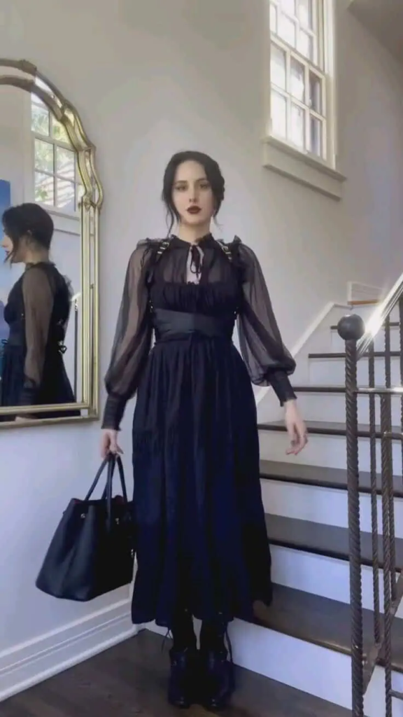 Flowing black midi dress with sheer sleeves paired with dark boots and minimalist accessories in a sophisticated boho goth look