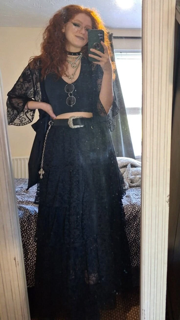 Sheer black lace kimono layered over a black crop top and flowing skirt with silver jewelry in a boho goth layered outfit