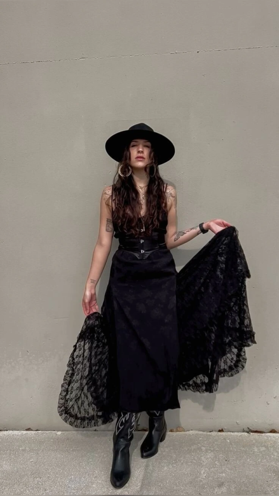 Black lace shawl draped over a fitted corset, styled with black cowboy boots and wide-brimmed hat in a boho goth outfit