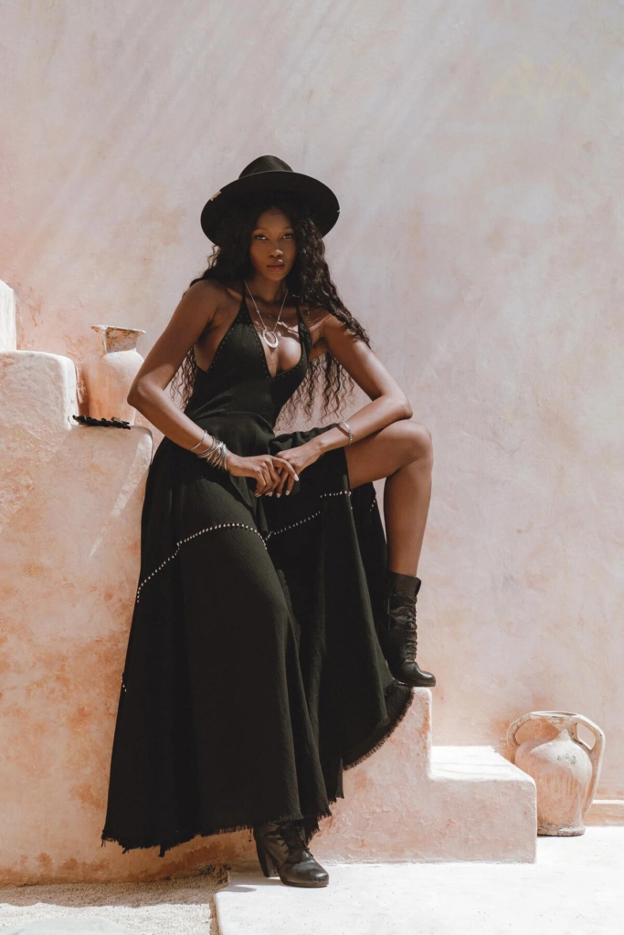 Black halter-neck dress with stud embellishments paired with lace-up boots and wide-brimmed hat in a boho goth outfit