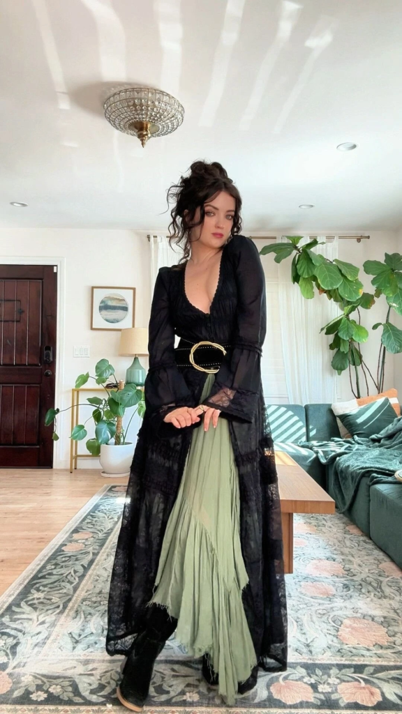 Sheer black lace duster cardigan over sage green pleated maxi skirt with gold belt and black boots in a boho goth outfit
