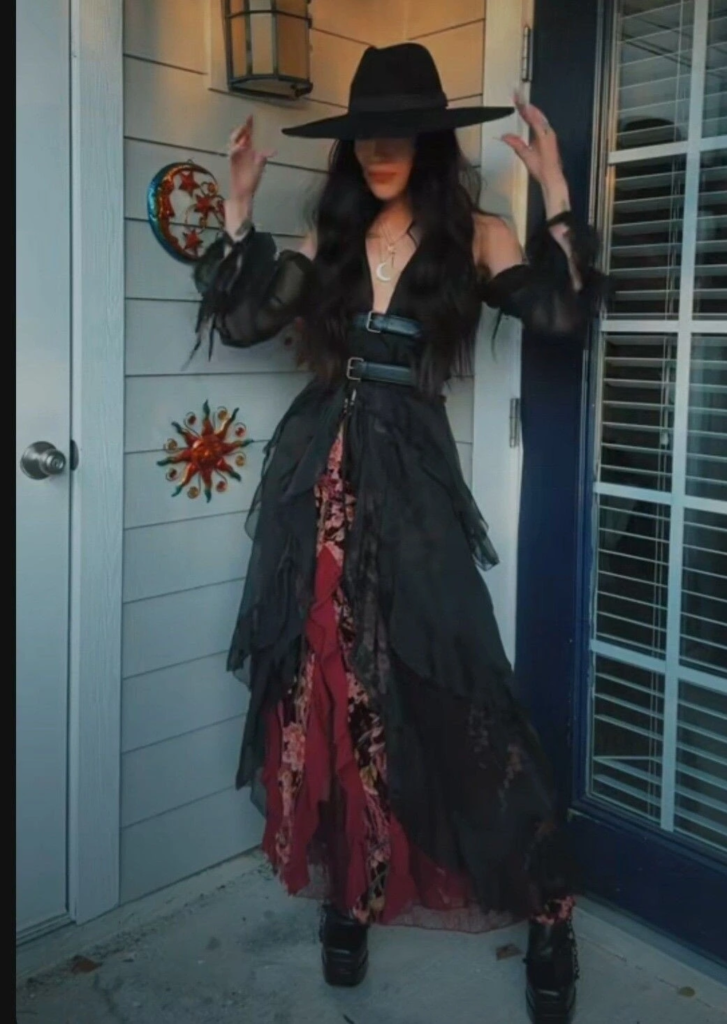 Sheer black cardigan layered over burgundy floral dress with wide-brimmed black hat and platform boots in a boho goth outfit